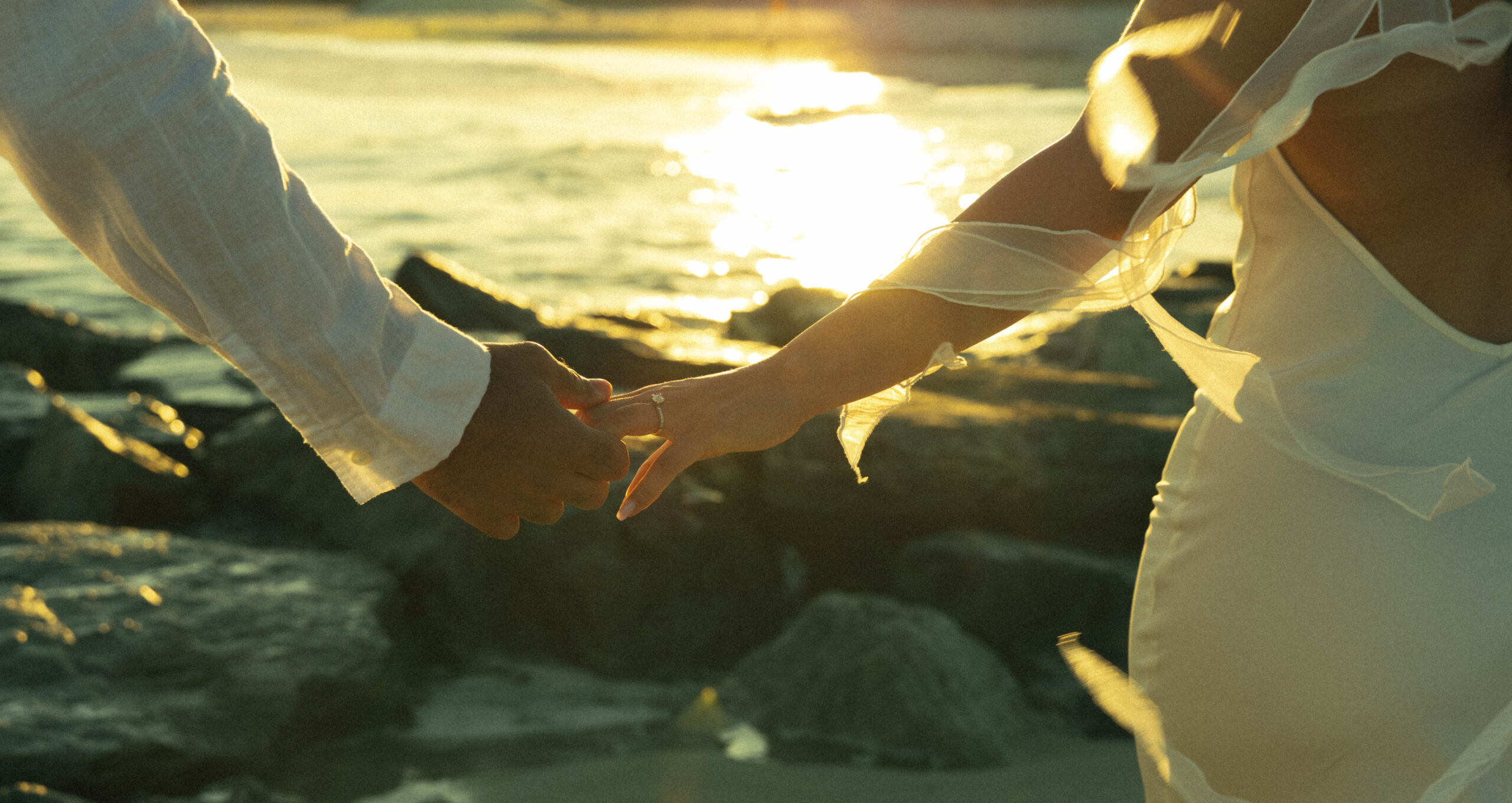 Couple holding hands on rocks by the water at sunset