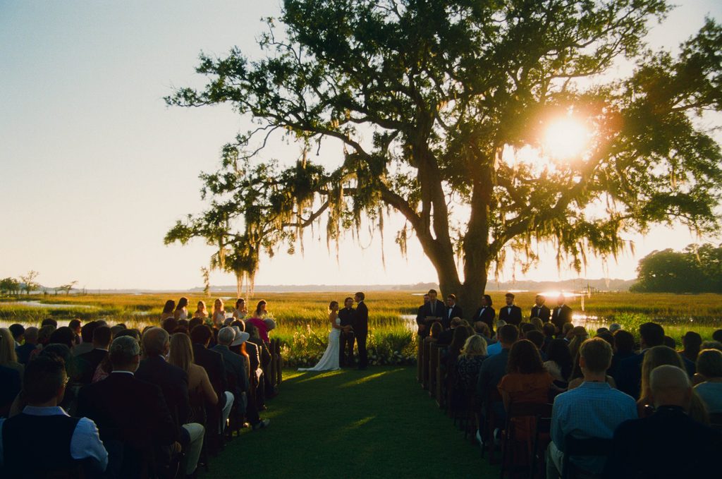 Outdoor wedding ceremony beneath a moss-draped live oak at sunset on the Charleston marsh