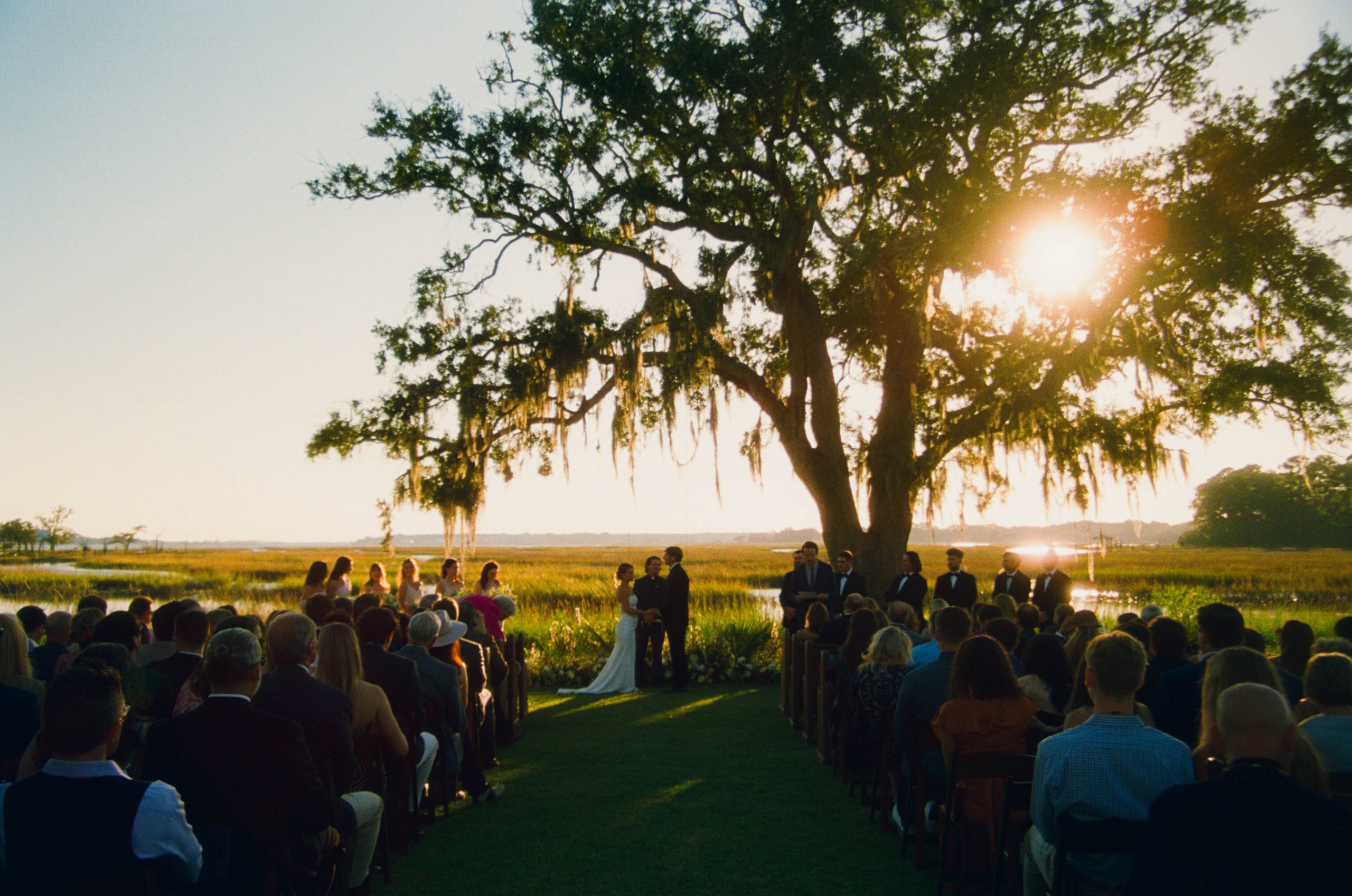 Outdoor wedding ceremony beneath a moss-draped live oak at sunset on the marsh