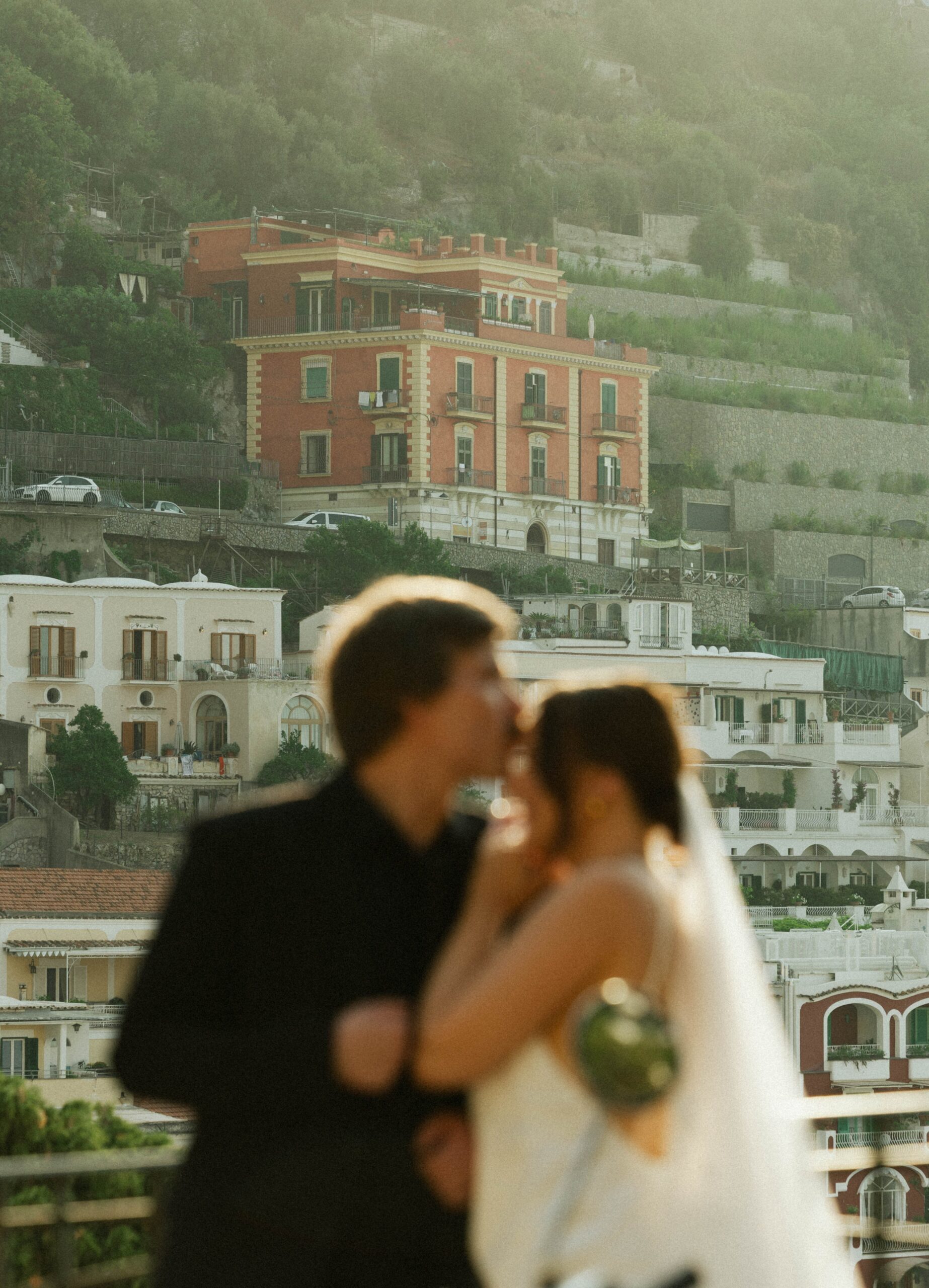 Groom kissing his bride with the pastel hillside villas of the Amalfi Coast behind them during an Italy destination wedding