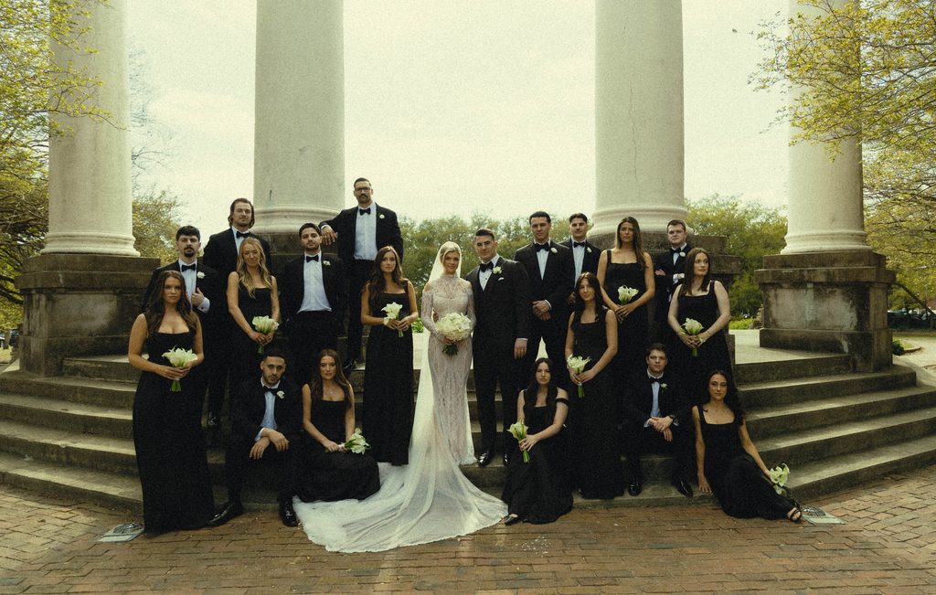 Bride and groom with their wedding party in black on the steps of a columned pavilion