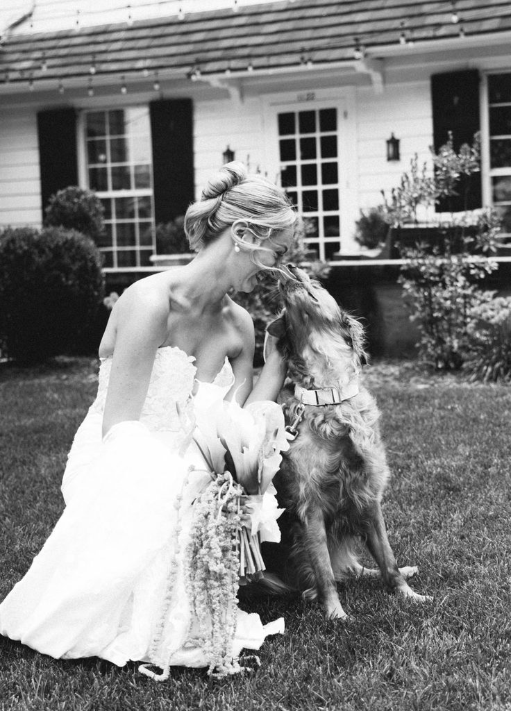 Black and white photo of Bethany in her wedding dress hugging her dog Honey on the lawn at The Morehead Inn in Charlotte, NC