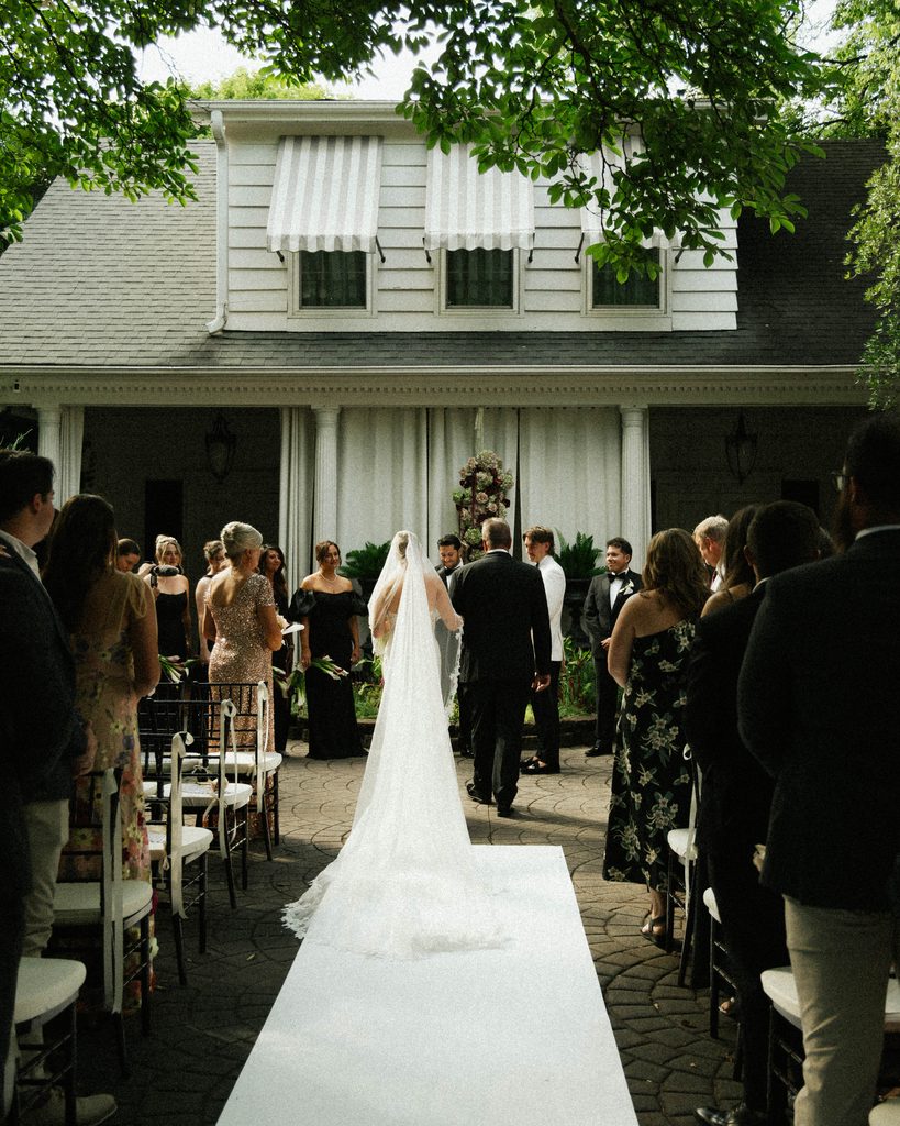 Bride walking down the aisle toward the groom in the brick courtyard at The Morehead Inn, Charlotte NC
