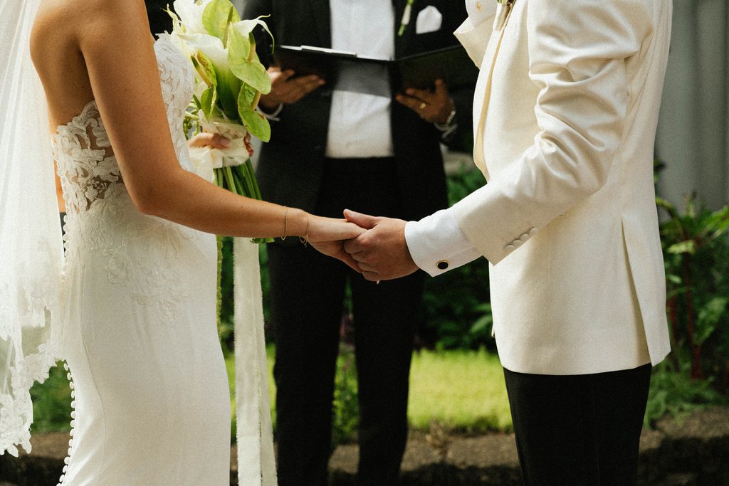 Bethany and Ethan holding hands during their courtyard wedding ceremony at The Morehead Inn
