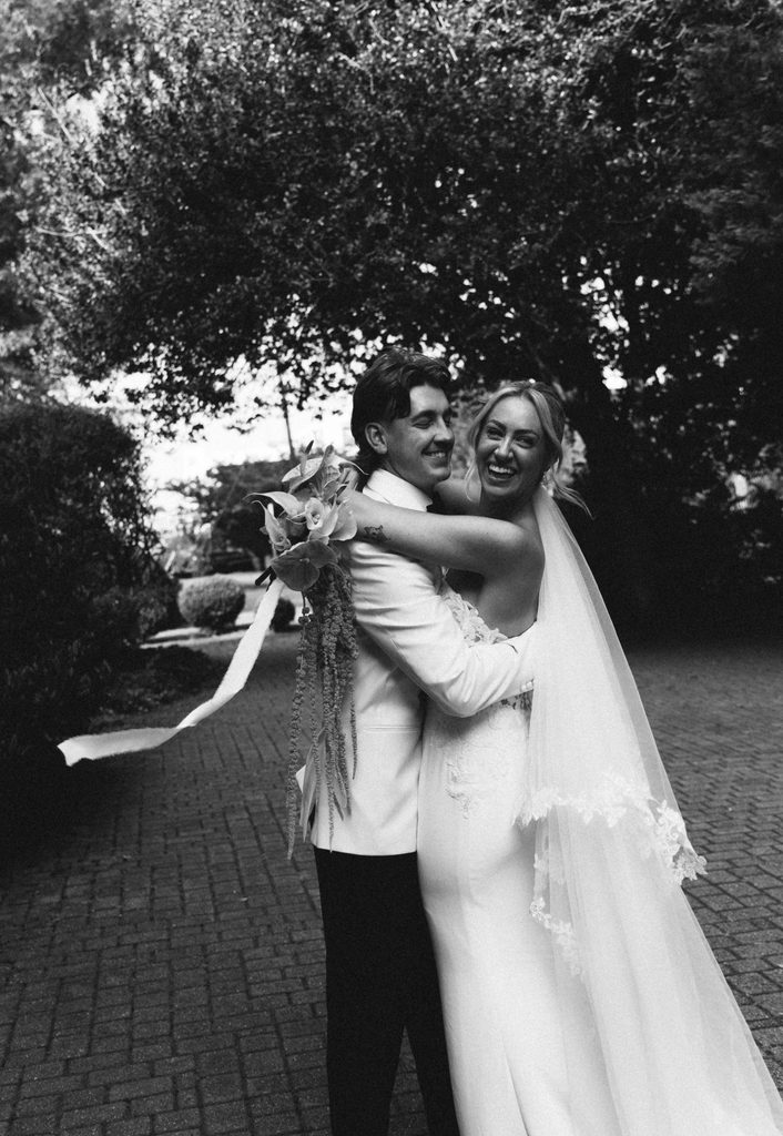 Black and white photo of Ethan hugging a laughing Bethany in the garden at The Morehead Inn, Charlotte wedding