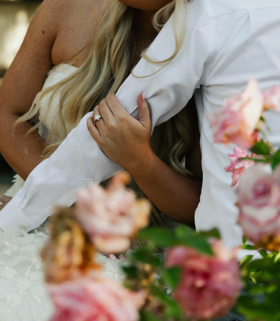 Close-up of a bride embracing her groom with pink roses in the foreground