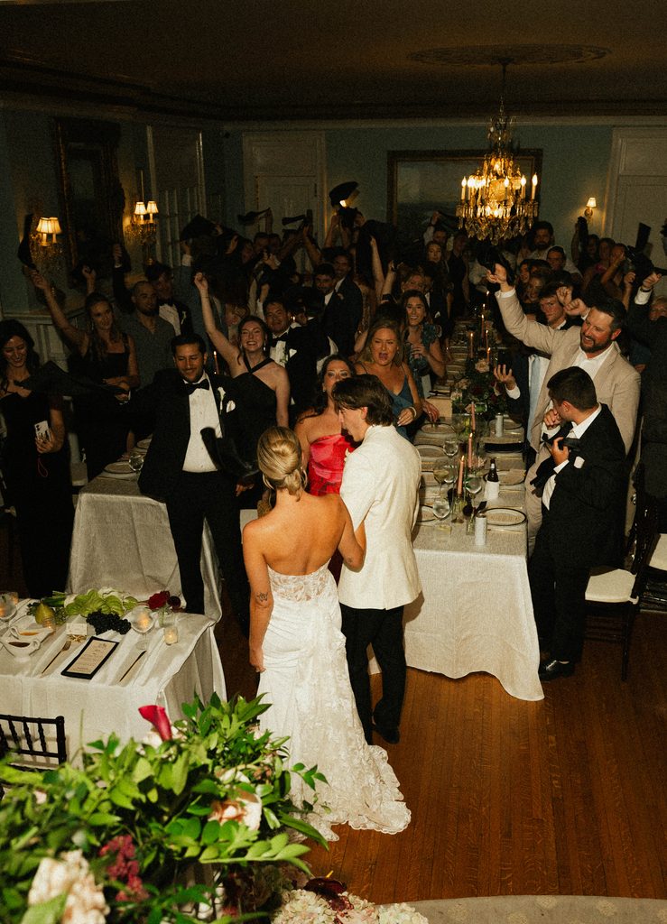 Bethany and Ethan dancing as guests cheer at their reception under the chandeliers at The Morehead Inn in Charlotte