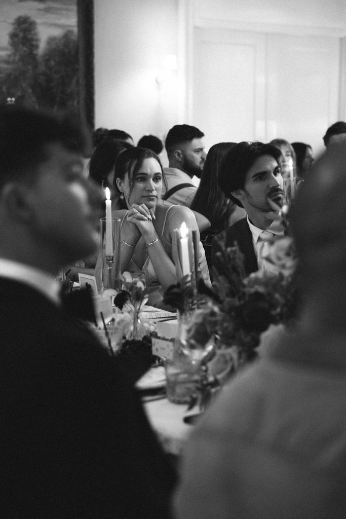 Black and white photo of wedding guests at candlelit dinner tables inside The Morehead Inn