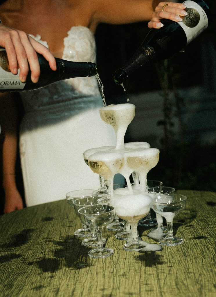 Bethany and Ethan pouring champagne into a coupe tower at their wedding reception at The Morehead Inn in Charlotte