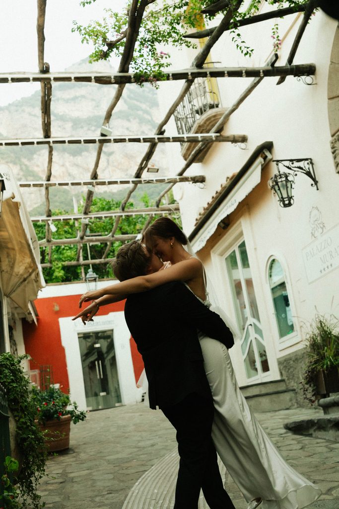 Groom lifting his bride under a vine-covered pergola during their Positano elopement