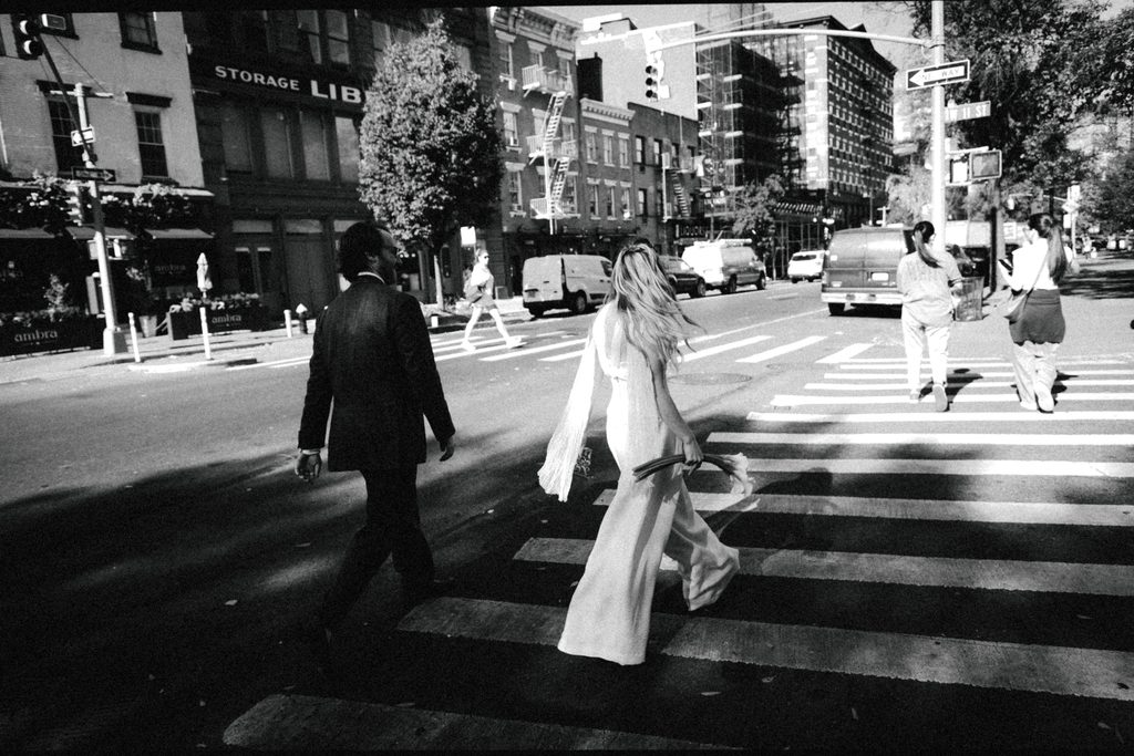 Black and white photo of Lauren and Jack crossing a New York City street, Lauren in a wide-leg bridal jumpsuit