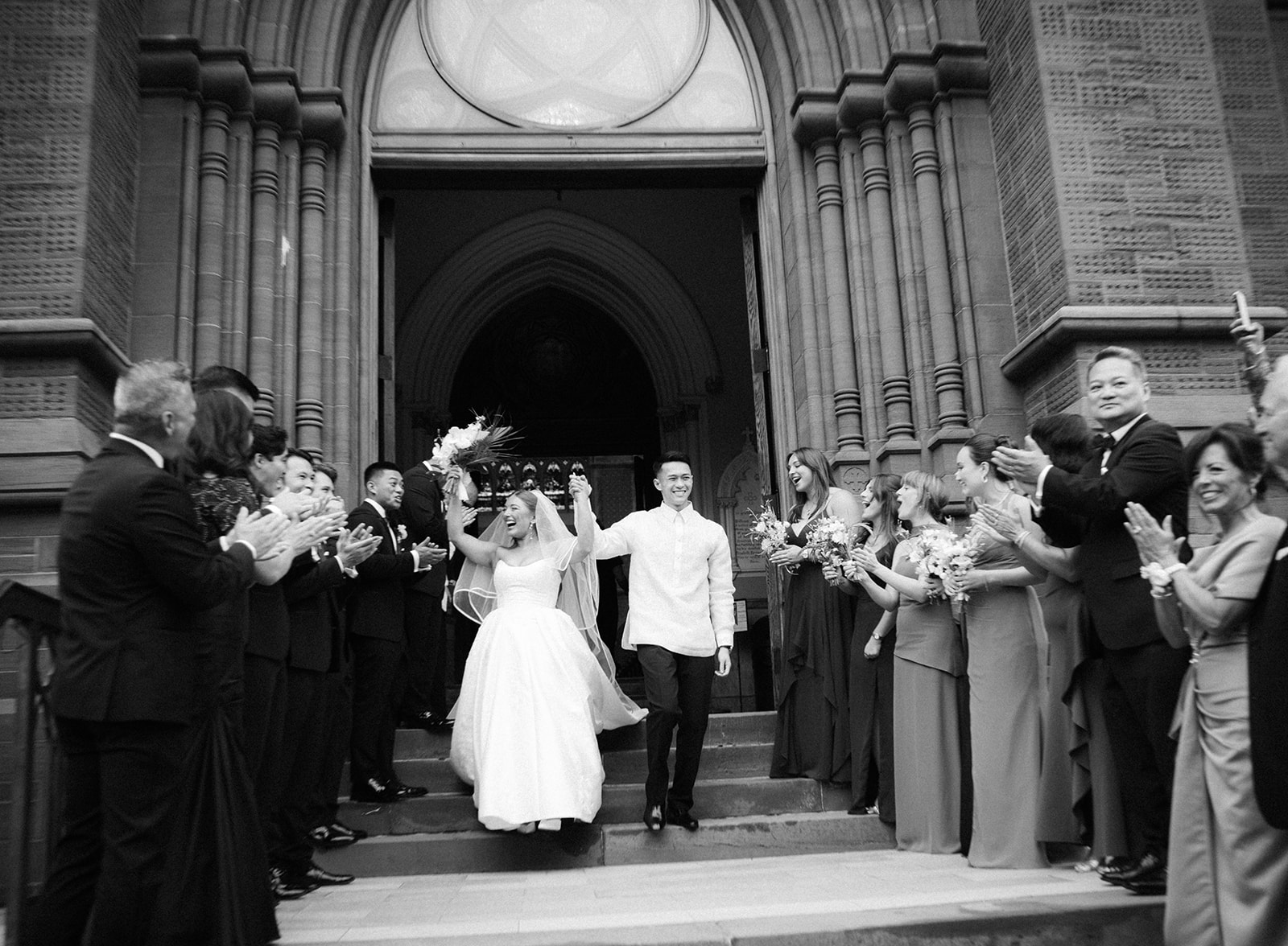 Bride and groom celebrating as they exit a historic cathedral while guests cheer, by a Charleston wedding photographer