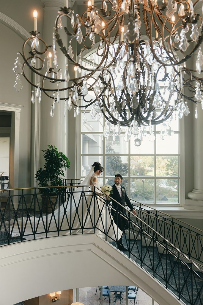 Bride and groom walking up the grand staircase beneath a crystal chandelier at The Ballantyne Hotel in Charlotte, NC