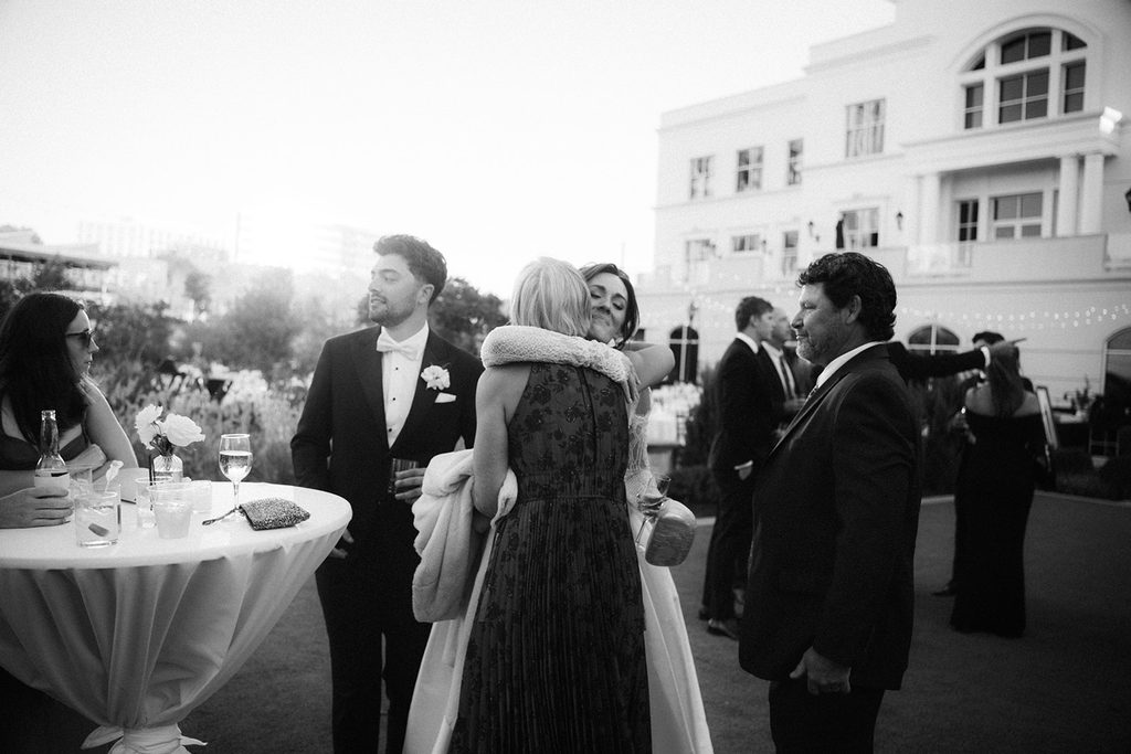 Black and white photo of a bride hugging a guest during cocktail hour